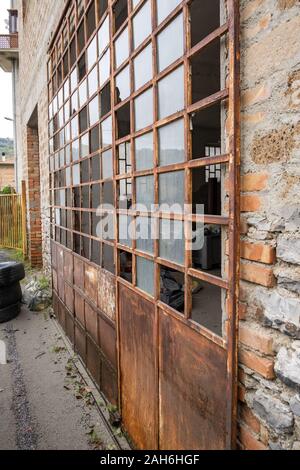 The broken windows and rusting frame of a door leading into a garage, nobody in the image Stock Photo