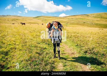 girl with a large backpack and a helmet with glasses in the field Stock Photo