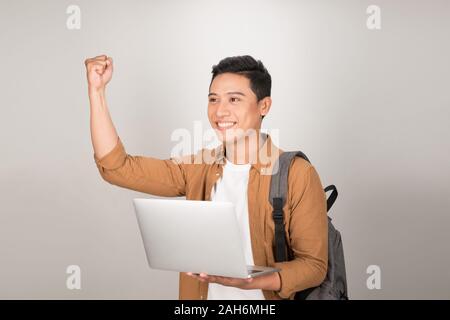 Young Asian guy celebrating passing entrance exams checking list of students online on laptop Stock Photo