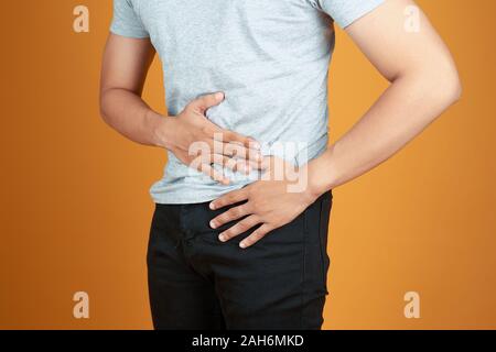 Close-up Of Young Man Suffering From Stomach Ache standing against orange background Stock Photo
