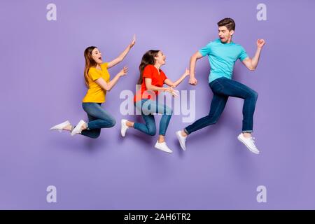 Full size body side profile view photo of one unhappy shocked guy running, away from two obsessive addicted ladies isolated violet background Stock Photo