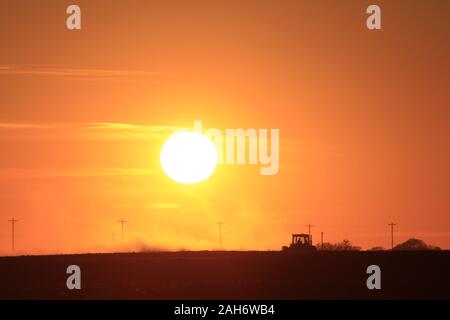 Blazing orange Kansas Sunset with a Farmer working his field out in the country in Kansas. Stock Photo