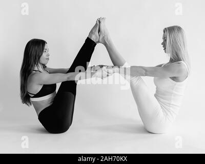 monochrome portrait of blonde and brunette beautiful cheerful fit women doing yoga asanas. Healthy lifestyle, Yin and Yang and sport concept Stock Photo