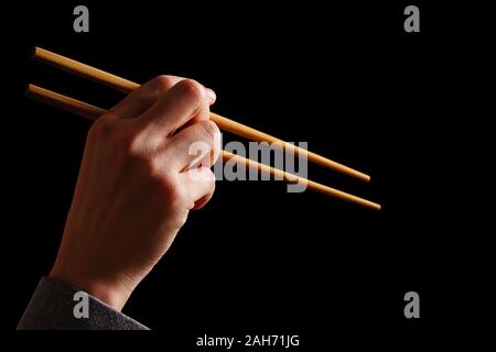 Female hand with wooden chopsticks. Hand holding traditional sushi bamboo sticks for Chinese, Japanese or Asian food, isolated on black background Stock Photo