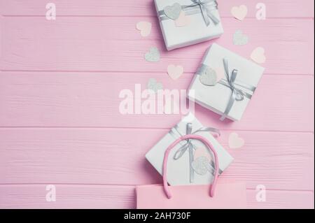Gift white boxes with silver satin ribbon from pink package and confetti in form of heart on pink background. Mock up on Womens Day, Valentines day Stock Photo