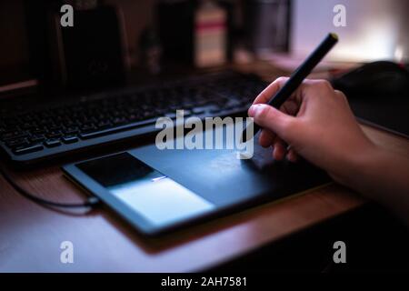 A man using graphic tablet with pen working on new project idea in the dim light of the monitor Stock Photo