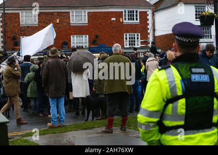 Tenterden, Kent, UK. 26 December, 2019. The annual Boxing Day meet of the Ashford Valley Tickham Hunt is taking place in the centre of Tenterden in Kent. Hounds and horses congregate at ‘The Vine Inn’ pub at 11am before heading down the high street to a packed audience. The weather is wet with drizzly rain. Police officer watches the crowd. ©Paul Lawrenson 2019, Photo Credit: Paul Lawrenson/Alamy Live News Stock Photo