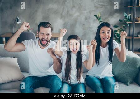 Portrait of nice attractive lovely charming cheerful cheery overjoyed, family mommy daddy wearing casual white t-shirts sitting on divan having fun ho Stock Photo
