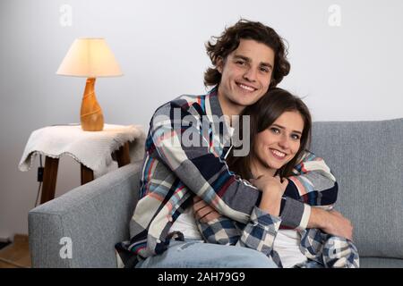 Smiling young man embracing girlfriend on couch. Stock Photo