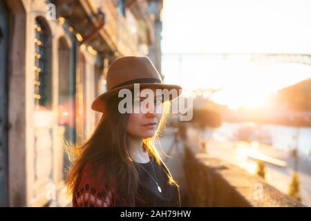 People, travel, holidays and adventure concept. Young woman with long hair walking on city street at sunrise, wearing hat and coat, enjoying happy ple Stock Photo