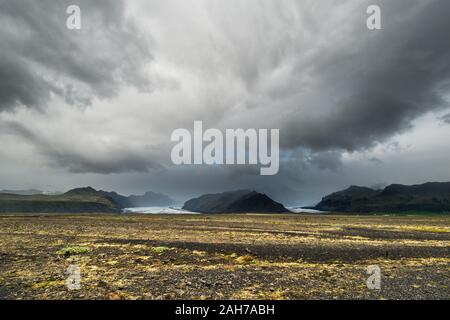 Icelandic landscape with a rocky desert in the foreground, and distant mountains with a glacier in the background, under a menacing cloudy sky Stock Photo