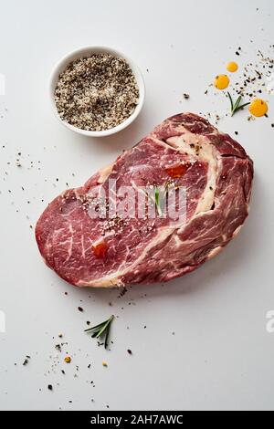 Fresh uncooked slab of seasoned beef steak with spice rub in a bowl to the side on a studio background with copy space viewed high angle Stock Photo