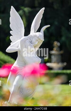 In a garden, a marble statue of Cupid and Psyche lies among flowers and hedges Stock Photo