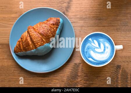 Cup of fresh blue art matcha and croissant on wooden background. Stock Photo