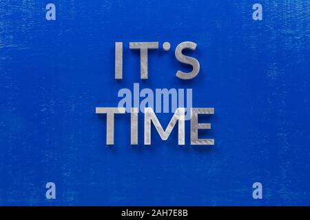The phrase it's time laid on blue painted board with thick silver metal aphabet characters. Stock Photo