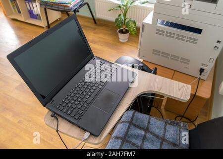 Open black laptop computer on a small chair table in office interior. Stock Photo