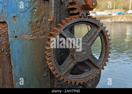 Close up of old manual boat lifting machine in harbour, showing rusted wheel and cog with water and boats blurred in background Stock Photo
