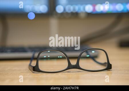 Closeup of protective glasses on an empty desk with blurred computer screen on background. Stock Photo