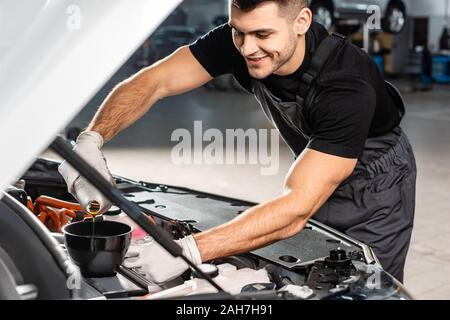 selective focus of smiling mechanic pouring oil to car engine Stock Photo