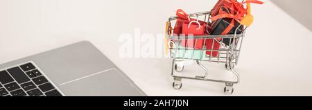 Toy gift boxes in cart beside laptop on table, panoramic shot Stock Photo