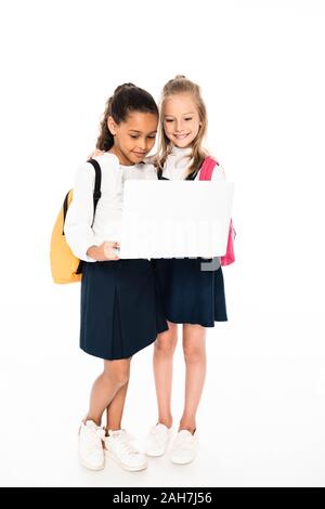 full length view of two multicultural schoolgirls using laptop isolated on white Stock Photo