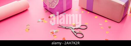 valentines confetti, scissors, wrapping paper, gift boxes on pink background, panoramic shot Stock Photo