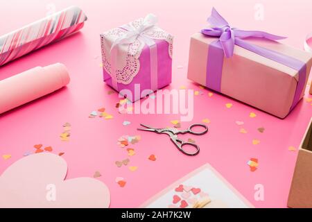 valentines confetti, scissors, wrapping paper, gift boxes on pink background Stock Photo