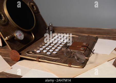 steampunk laptop, glasses and documents on wooden table isolated on grey Stock Photo