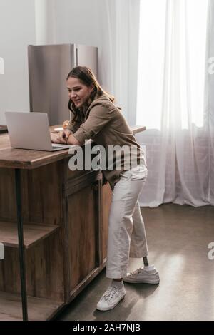 Beautiful girl with prosthetic leg using laptop with blank screen