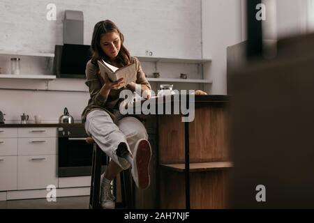 Beautiful young woman with prosthetic leg reading book on sofa in