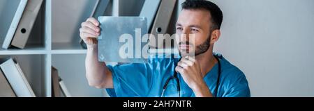 panoramic shot of handsome orthopedist looking at x-ray Stock Photo