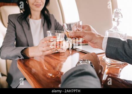 cropped view of businessman and businesswoman toasting glasses with alcohol in private jet Stock Photo