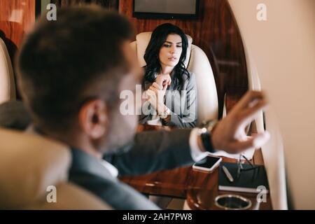 selective focus of worried businesswoman with fear of flight sitting with businessman in private jet Stock Photo
