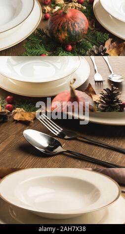 collage of white ceramic plates, cutlery, fir, cones among pumpkins on wooden table, Thanksgiving festive table setting Stock Photo