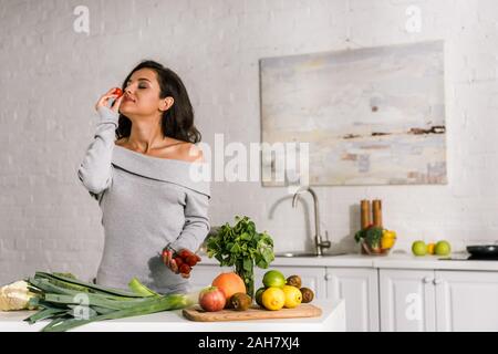 attractive girl smelling cherry tomato near vegetables Stock Photo