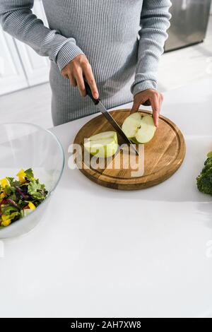 cropped view of woman holding knife near halves of apple Stock Photo