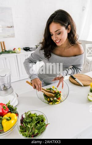 happy girl mixing fresh salad near vegetables at home Stock Photo