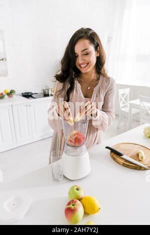 happy pregnant woman putting banana in blender with grapefruit Stock Photo