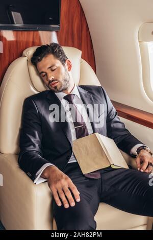 handsome businessman in suit with book sleeping in private plane Stock Photo
