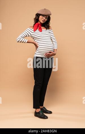 pregnant french woman in beret looking at camera on beige background Stock Photo