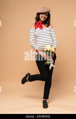 pregnant french woman in beret holding bouquet on beige background Stock Photo