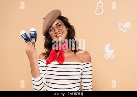 pregnant french woman in beret holding sneakers on beige background Stock Photo