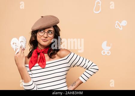 pregnant french woman in beret holding shoes on beige background Stock Photo