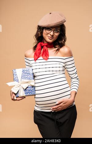 pregnant french woman in beret holding gift isolated on beige Stock Photo