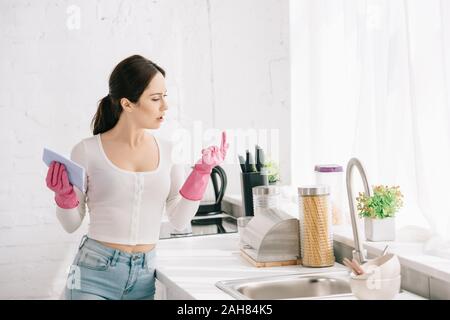 young housewife standing in kitchen in rubber gloves and holding rag Stock Photo