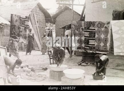 Gold CoastGhana, Women and children wash clothes outdoors at an Asante (Ashanti) village. Large squares of patterned cloth are hung up to dry on a washing line behind them. Original manuscript caption: A village in Western Ashanti, washing day, 1951-52. 1995/076/5/2/2/28. Stock Photo