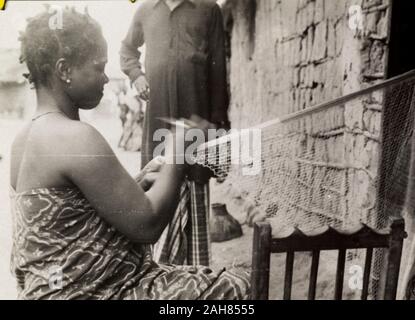 gold coastghana a ghanaian woman in traditional dress sits outside a mud walled building as she repairs fishing nets original manuscript caption a net mender 1951 52 199507652235 2ah8555