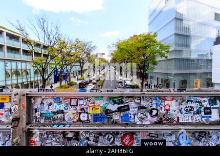 Omotesando Hills shopping complex in Central Tokyo on left, Omotesando Avenue, and Dior building on the right. Seen from bridge covered in stickers. Stock Photo