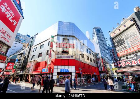 Wide angle shot of the Sega games store in Shinjuku, Tokyo with the Mode Gakuen Cocoon Tower in the background. Foreground street busy with people. Stock Photo