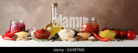 Set of different delicious sauces, olive oil, garlic, tomato cherry on white table against brown background, space for text Stock Photo